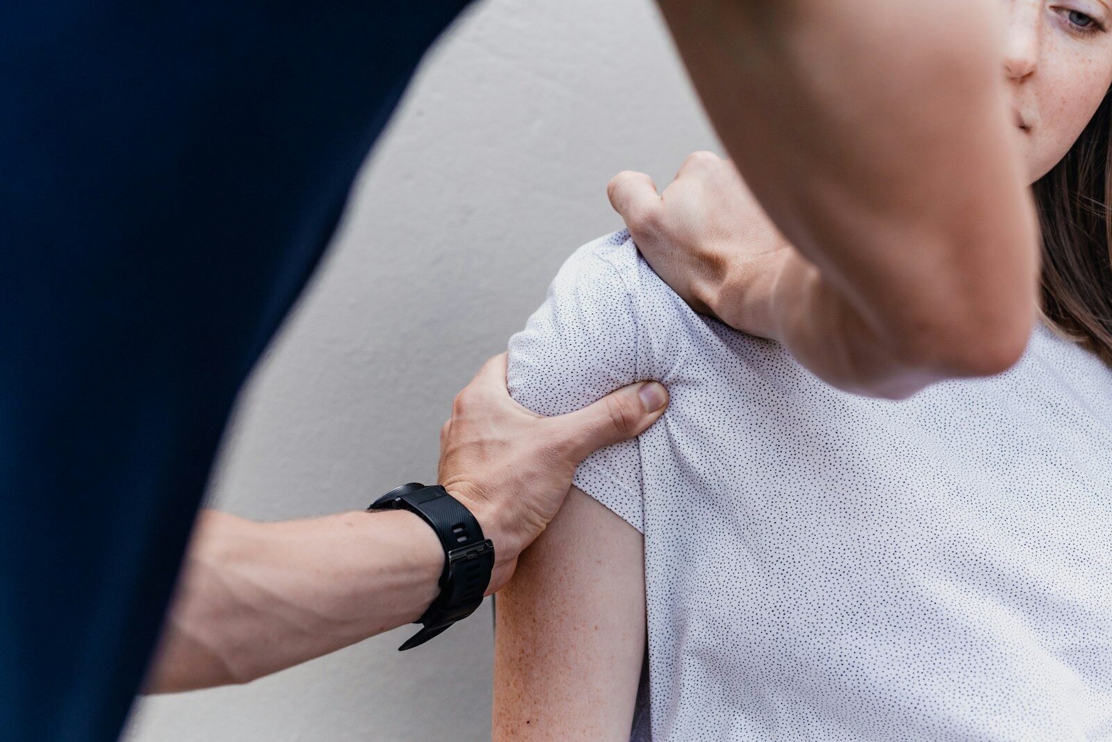 A person massaging the shoulder of another person wearing a white patterned shirt